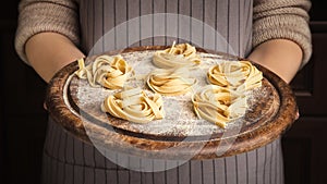 Woman chef holding wooden tray with fettuccine nests