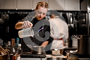 woman chef holds plastic measuring cup and pours liquid into saucepan