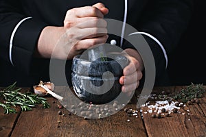 Woman chef pounding spices and herbs in mortar for food cooking on a black background