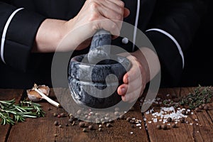 Woman chef pounding spices and herbs in mortar for food cooking on a black background