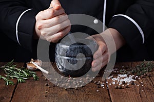 Woman chef pounding spices and herbs in mortar for food cooking on a black background