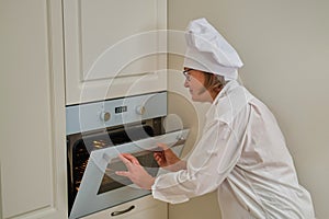 A woman in chef`s clothes turns on the oven while cooking an apple pie in the kitchen