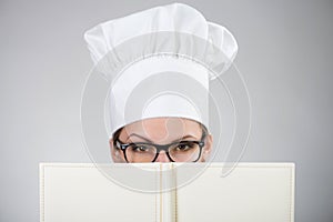 Woman in chef's hat looking over the cookbook