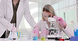 Woman chemist in gloves examines specimen using microscope