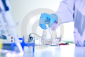 Woman chemist hand in plastic glove shaking laboratory beaker. Scientific Lab for Medicine, Biotechnology Researchers