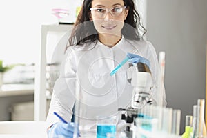 Woman chemist holds in hand a glass for test tube, with liquid solution of blue color