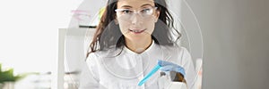 Woman chemist holds in hand a glass for test tube, with liquid solution of blue color