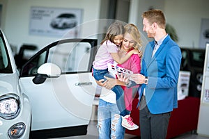 Woman with child in car dealership looking at brochure with sal