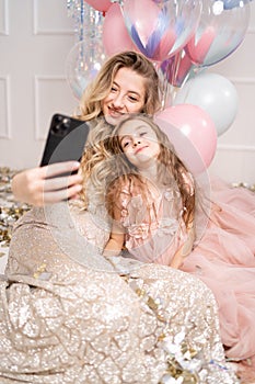 A woman and a child dressed in delicate pink dresses take a selfie against the backdrop of helium balloons.
