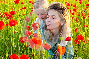 Woman with child girl in field with red poppies. Mother and daughter are playing in the field of flowering red poppies.