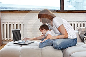 A woman with a child at a laptop sitting on a sofa. Work at home, freelancer, work during maternity leave for remote