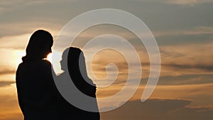 A woman with a child looks forward to the sunset, the view from behind