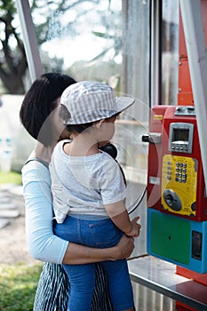 Woman and child Mother and Kid Boy Baby using oldstyle public  pay phone in telephone booth