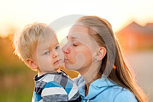 Woman and child outdoors at sunset. Mother kissing her son.