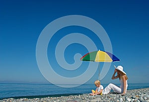 Woman and child sit under an umbrella