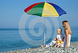 Woman and child sits under an umbrella