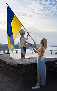 woman and child with Ukrainian flag stand on roof of house