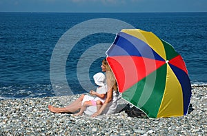 Woman with child under umbrella on coast