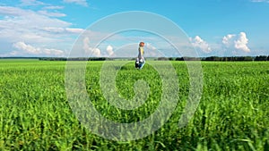 A woman with a child walk along the road along green fields of young wheat shoots against a blue sky with white feathery clouds