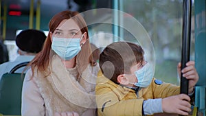 Woman with child wearing medical masks observes modern precautions in public while riding city bus