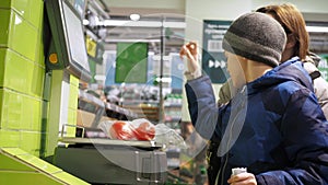 A woman with a child weighs tomatoes in a store on a scale. A showcase with products. Supermarket grocery, retail