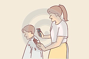 Woman children hairdresser cuts little boy hair and holds trimmer and comb in hands