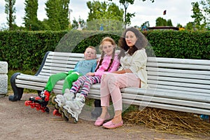 Woman with children on roller skates resting on a bench in the P