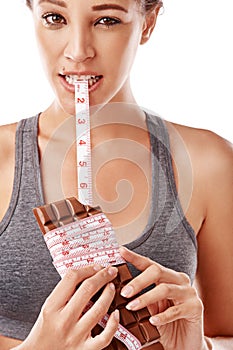 Woman, chocolate and bite with measuring tape for unhealthy diet with junk food in studio. Female person, eating and
