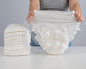 A woman chooses an adult diaper from a pile. Urinary incontinence problem.