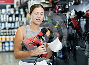 Woman chooses and buys paint spray gun in hardware store