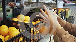 A woman chooses fresh oranges in the produce section of a grocery store and puts them in a plastic bag