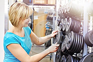 Woman chooses loads for dumbbell in shop