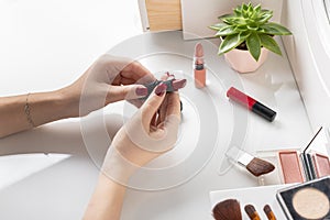 Woman chooses red lipstick to match the color of nail polish. Top view of dressing table with makeup accessories