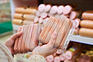 Woman chooses sausages in vacuum package at store