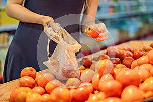 A woman chooses tomatoes in a supermarket without using a plastic bag. Reusable bag for buying vegetables. Zero waste