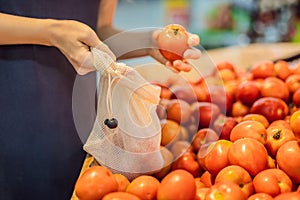 A woman chooses tomatoes in a supermarket without using a plastic bag. Reusable bag for buying vegetables. Zero waste