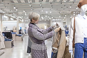 A woman chooses a warm jacket in a store. Seasonal change of collection. Style, fashion and beauty