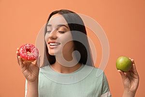 Woman choosing between apple and doughnut on orange background