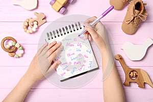 Woman choosing baby name at pink wooden table, top view