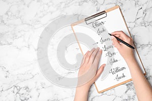 Woman choosing baby name at white marble table, top view. Space for text