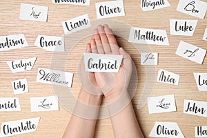 Woman choosing baby name at wooden table, top view