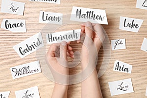 Woman choosing baby name at wooden table, top view