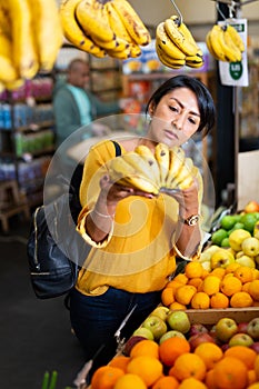 Woman choosing bananas in fruit and vegetable section of supermarket