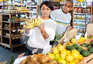 Woman choosing bananas in fruit and vegetable section of supermarket