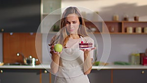 Woman choosing between cake and apple on kitchen. Woman choosing cake