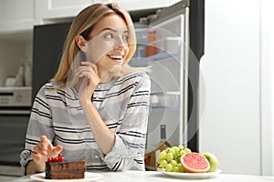 Woman choosing between cake and healthy fruits at table in kitchen