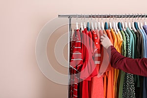 Woman choosing clothes from wardrobe rack on color background