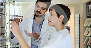 Woman choosing her new glasses at optics store with help of ophthalmologist