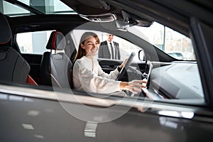 Woman choosing new car in dealership with salesman trying on new automobile