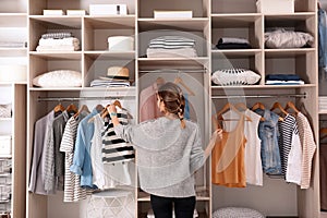 Woman choosing outfit from large wardrobe closet with stylish clothes